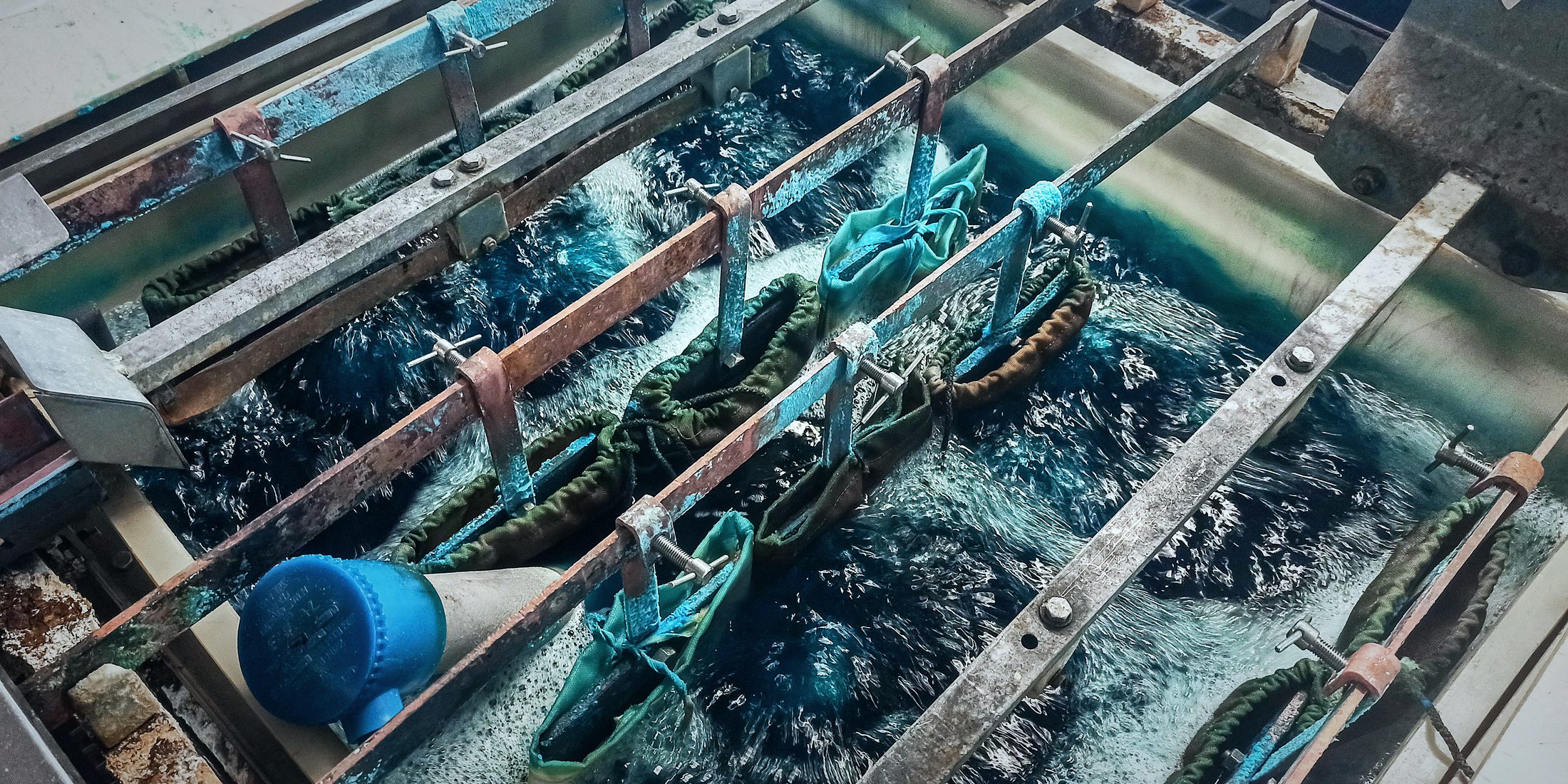 Parts in mesh bags submerged in an agitated blue plating bath, hanging from rack bars